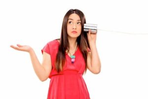 Confused young woman trying to talk on a tin can.